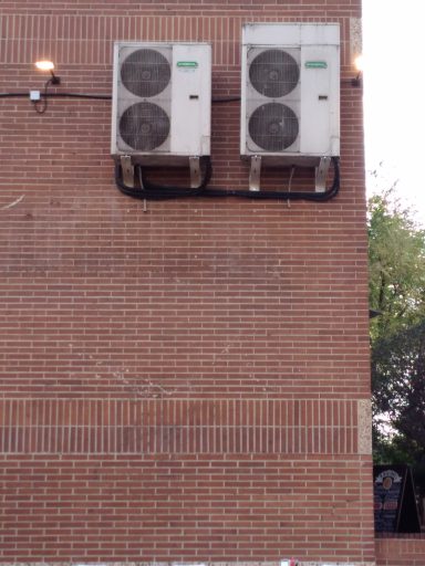 Dos unidades de aire acondicionado montadas en una pared de ladrillo.