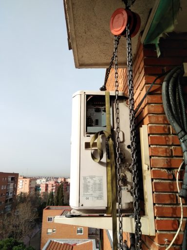 Unidad exterior de aire acondicionado colgada en un balcón, con una cadena de soporte.